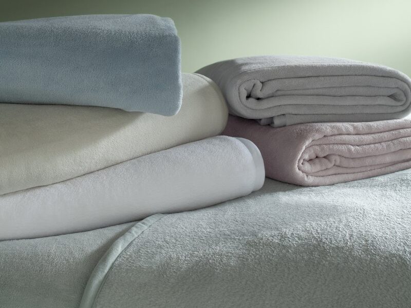 Cobertores Buddemeyer Aspen II dobrados em pilha, em tons de azul, branco, bege, cinza e rosa