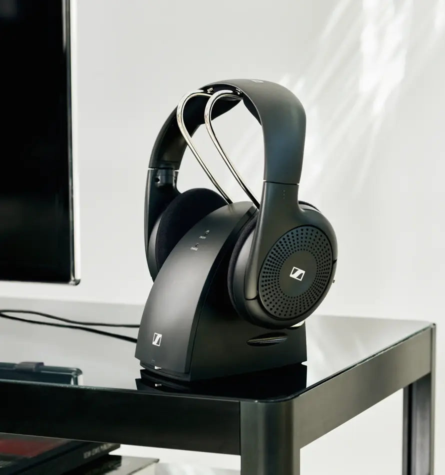 Fone sem fio Sennheiser RS 120-W preto apoiado na base transmissora, sobre uma mesa ao lado de uma TV