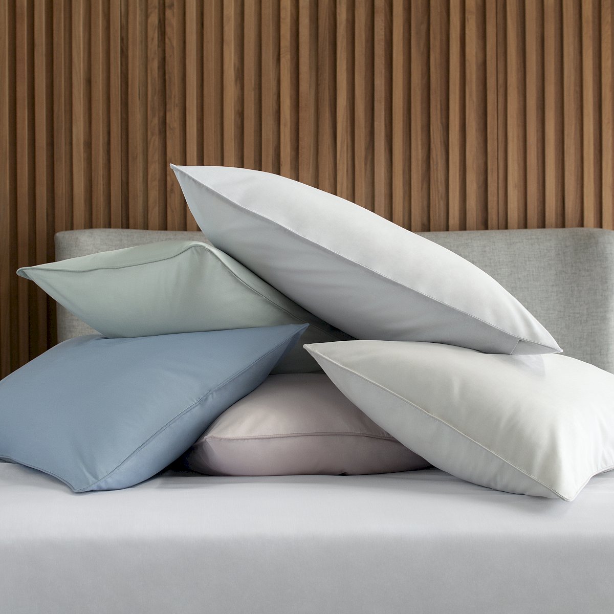Fronhas lisas da linha Basic Percalle da Buddemeyer em várias cores, empilhadas sobre a cama