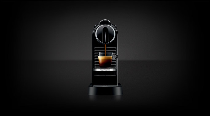 Cafeteira de cápsulas Nespresso CitiZ preta servindo café em uma xícara de vidro